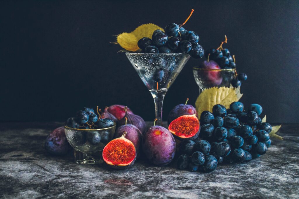 Dark moody still life of fresh grapes and figs in a glass setting, highlighting autumn flavors.